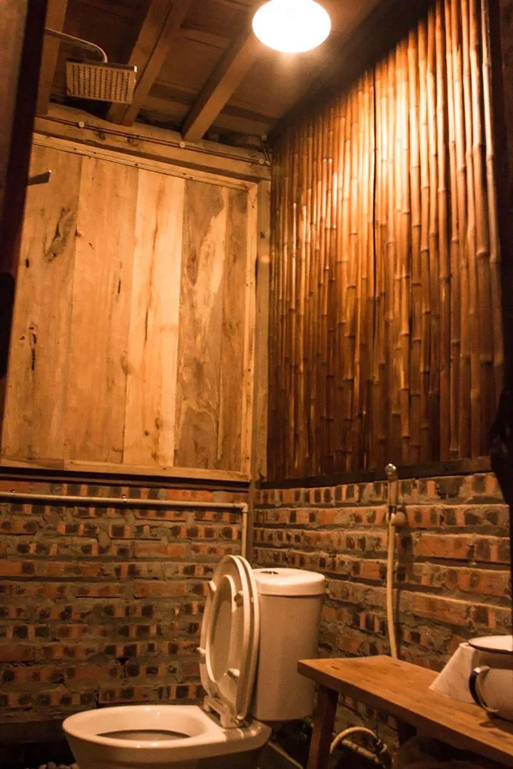 Ein rustikales Badezimmer mit Holzwand und Backsteinwand, sowie einer Toilette.
