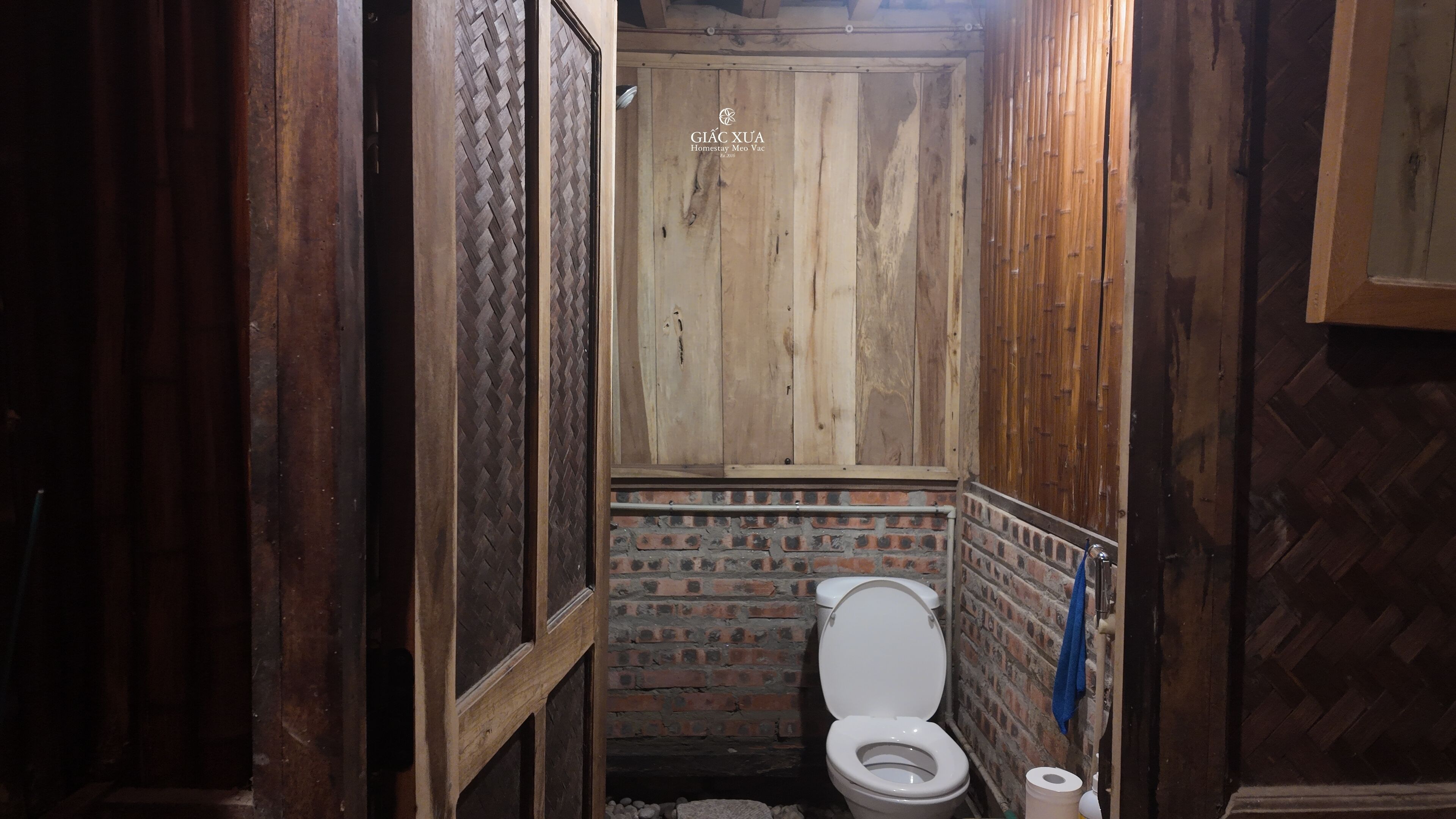 A rustic bathroom with a wooden door, a toilet, and a brick wall.