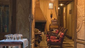 Un intérieur rustique avec des poutres en bois, une cheminée en pierre et une table en bois sur laquelle sont posés des verres.