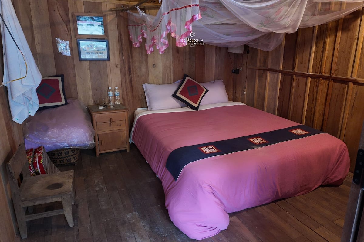 Une piĂšce en bois avec un lit, une table de chevet, un petit tabouret et une moustiquaire.