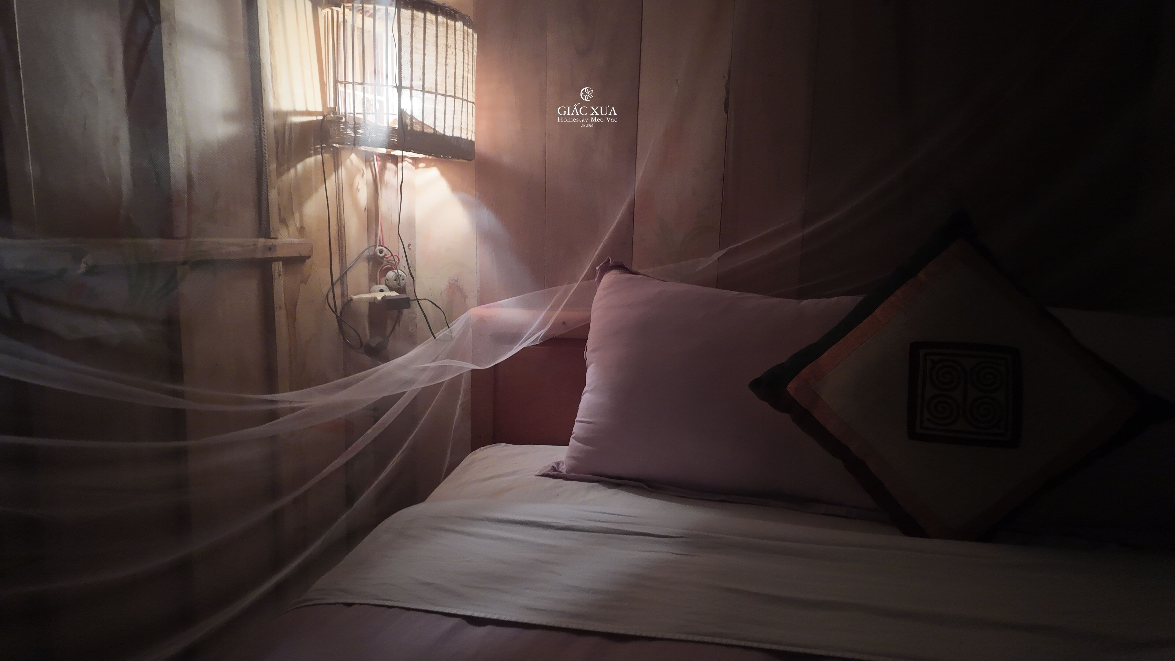 A bed with a mosquito net, a wall-mounted light fixture, and a pillow with a geometric design.