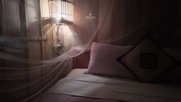 A bed with a mosquito net, a wall-mounted light fixture, and a pillow with a geometric design.