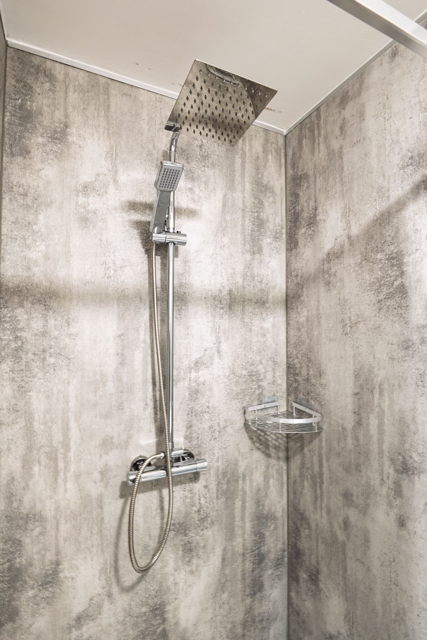 A shower with a handheld showerhead and a wall-mounted control panel.