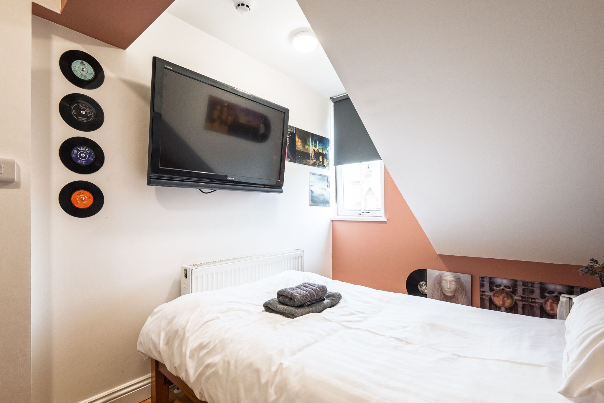 Une chambre à coucher avec un lit, un téléviseur à écran plat et un lecteur de disques fixé au mur.