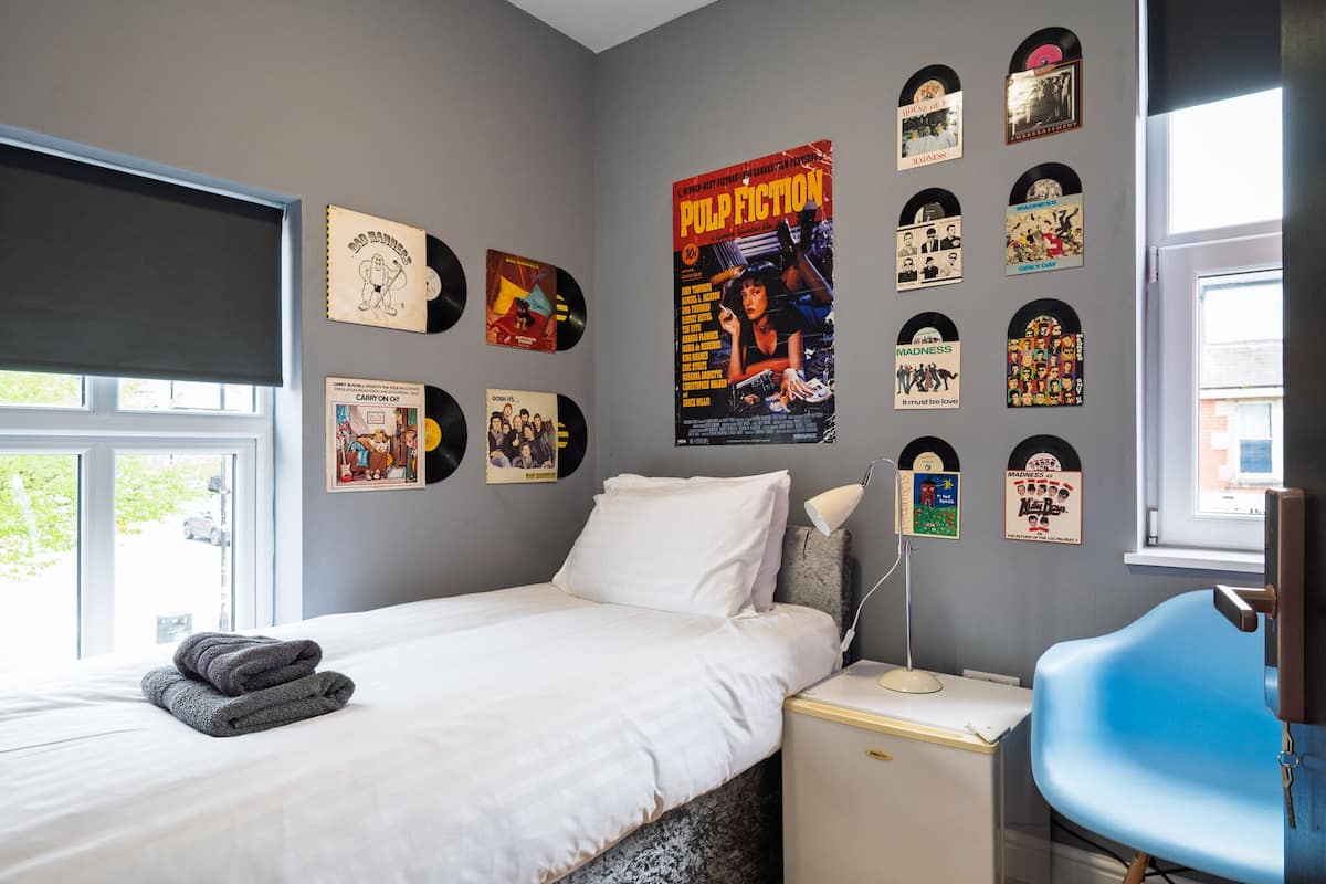 A bedroom with a bed, a desk, and a chair. There are vinyl records and a movie poster on the wall.