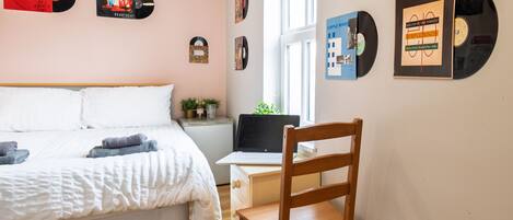 A bedroom with a bed, a wooden chair, a desk with a laptop, and a window.