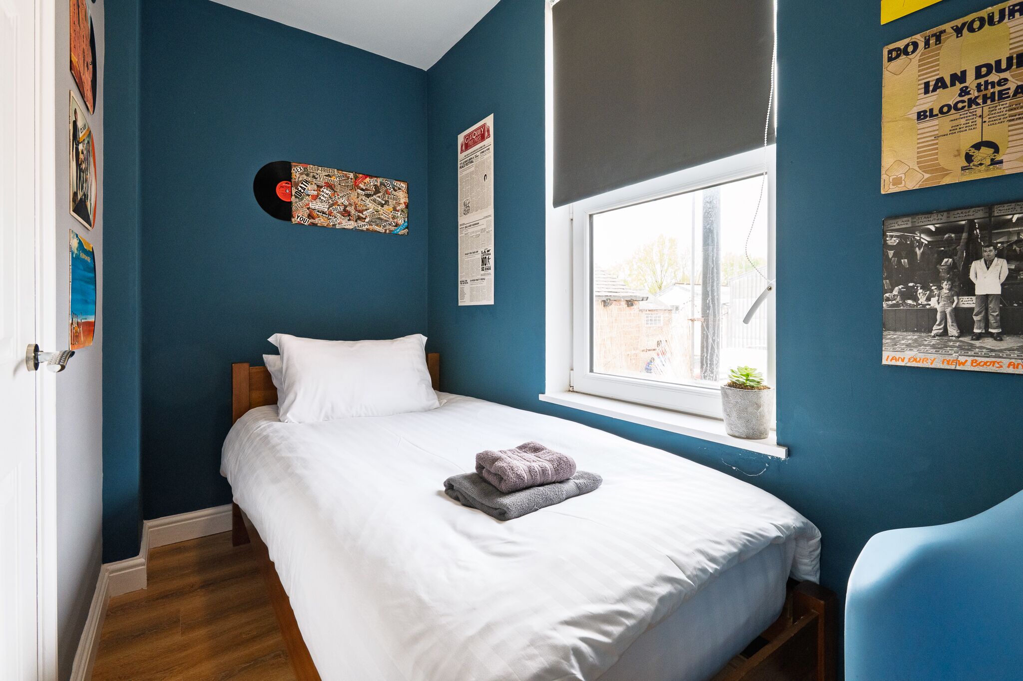 Un dormitorio con una cama, un ventanal y adornos en la pared, incluyendo un disco de vinilo y carteles.