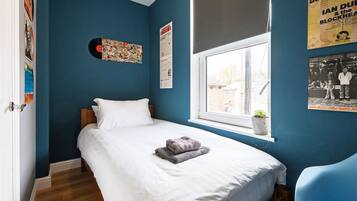 Un dormitorio con una cama, un ventanal y adornos en la pared, incluyendo un disco de vinilo y carteles.
