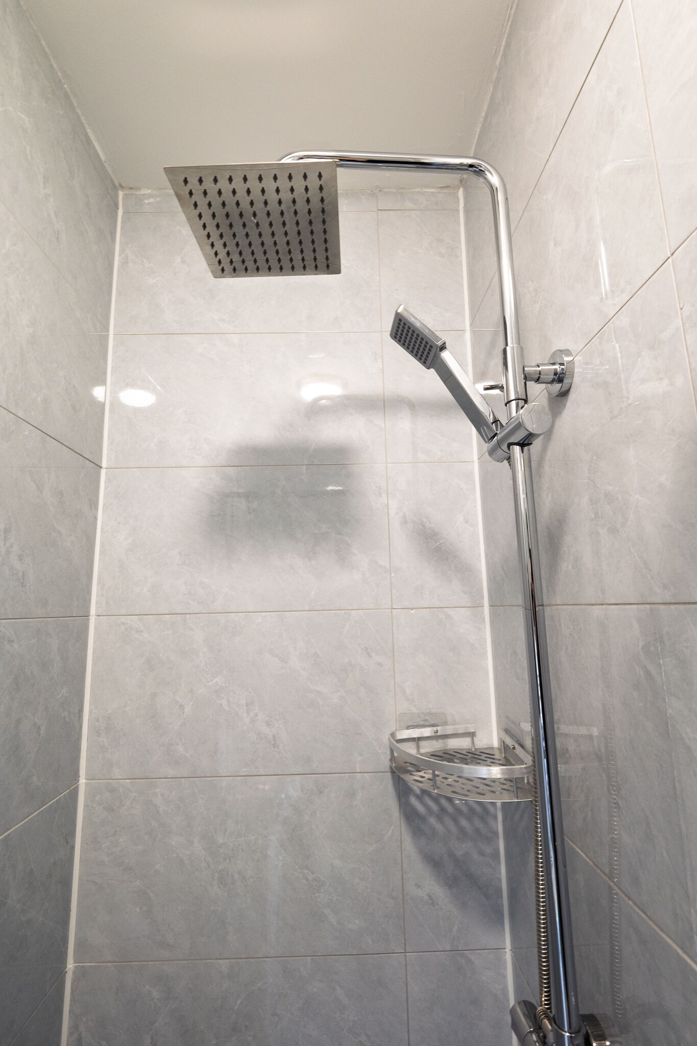 Eine Dusche mit einer eckigen Duschbrause und einer Handbrause, einer Glasduschtasse sowie Chromarmaturen.