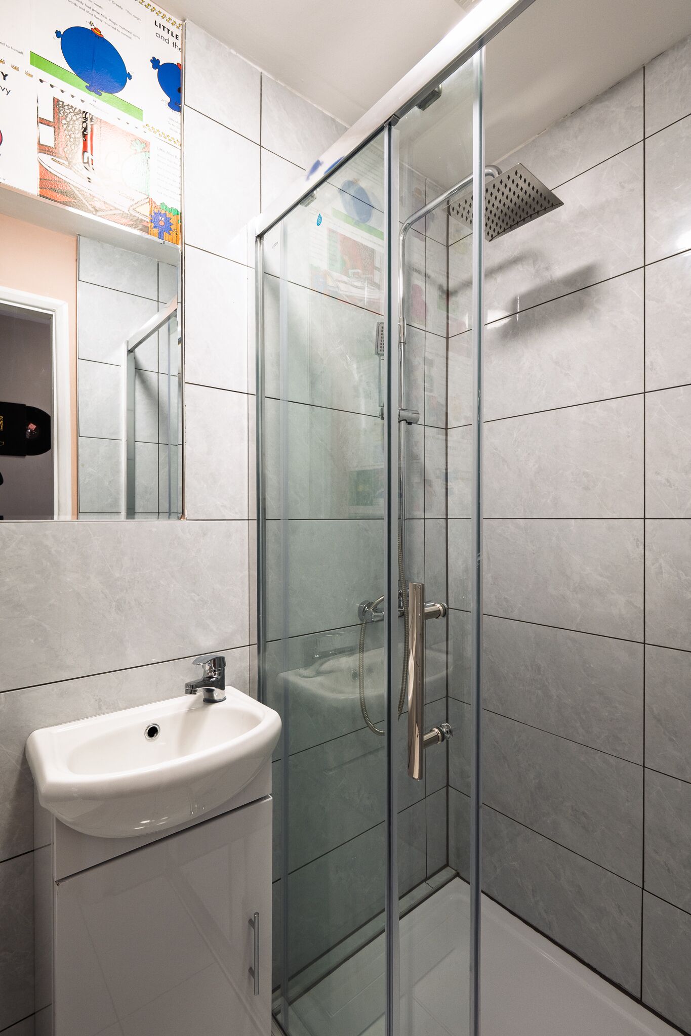 Un baño moderno con ducha envuelta en vidrio, un lavamanos blanco y un espejo sobre él.