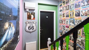 Um corredor com uma porta preta, uma placa da Rota 66 e uma parede coberta com diversas capas de revistas.