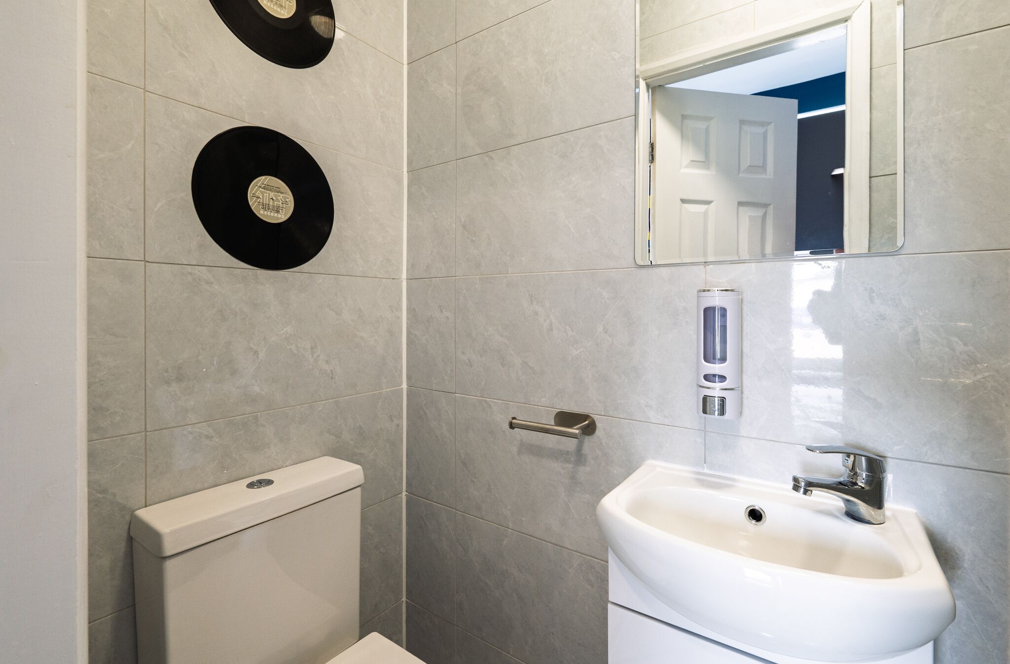 A bathroom with a toilet, sink, and two wall-mounted vinyl records.