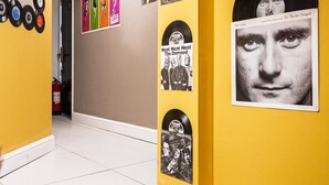 Um corredor com paredes amarelas, piso de madeira e diversos cartazes e discos de vinil expostos nas paredes.