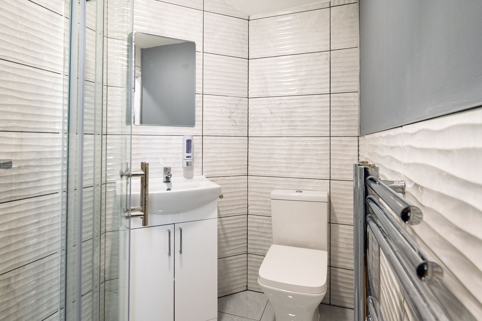 Un baño moderno con cabina de ducha de vidrio, un lavabo blanco y un inodoro.