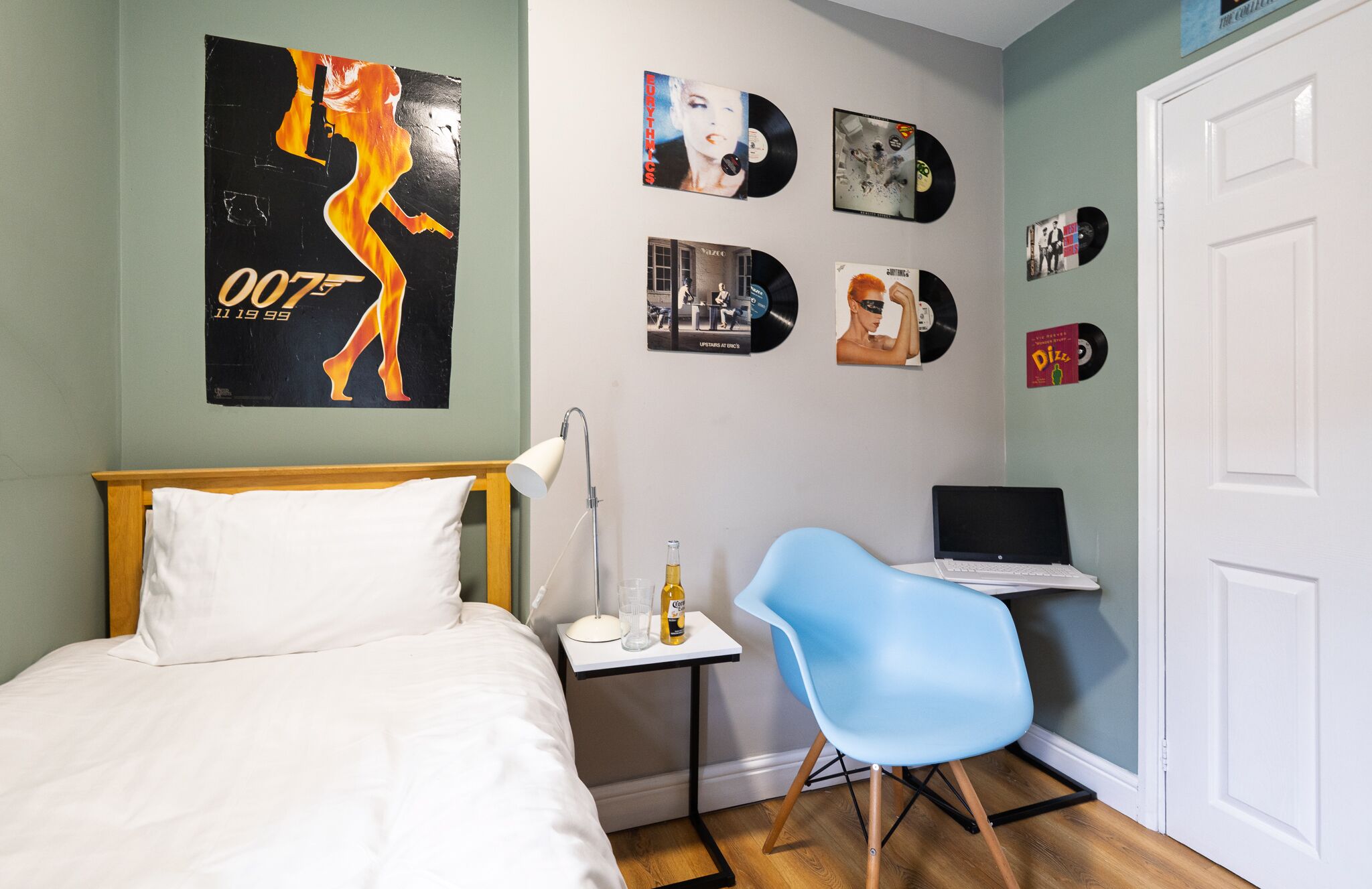 Een slaapkamer met een bed, een bureau met een laptop, een stoel en een muur versierd met vinylplaten.