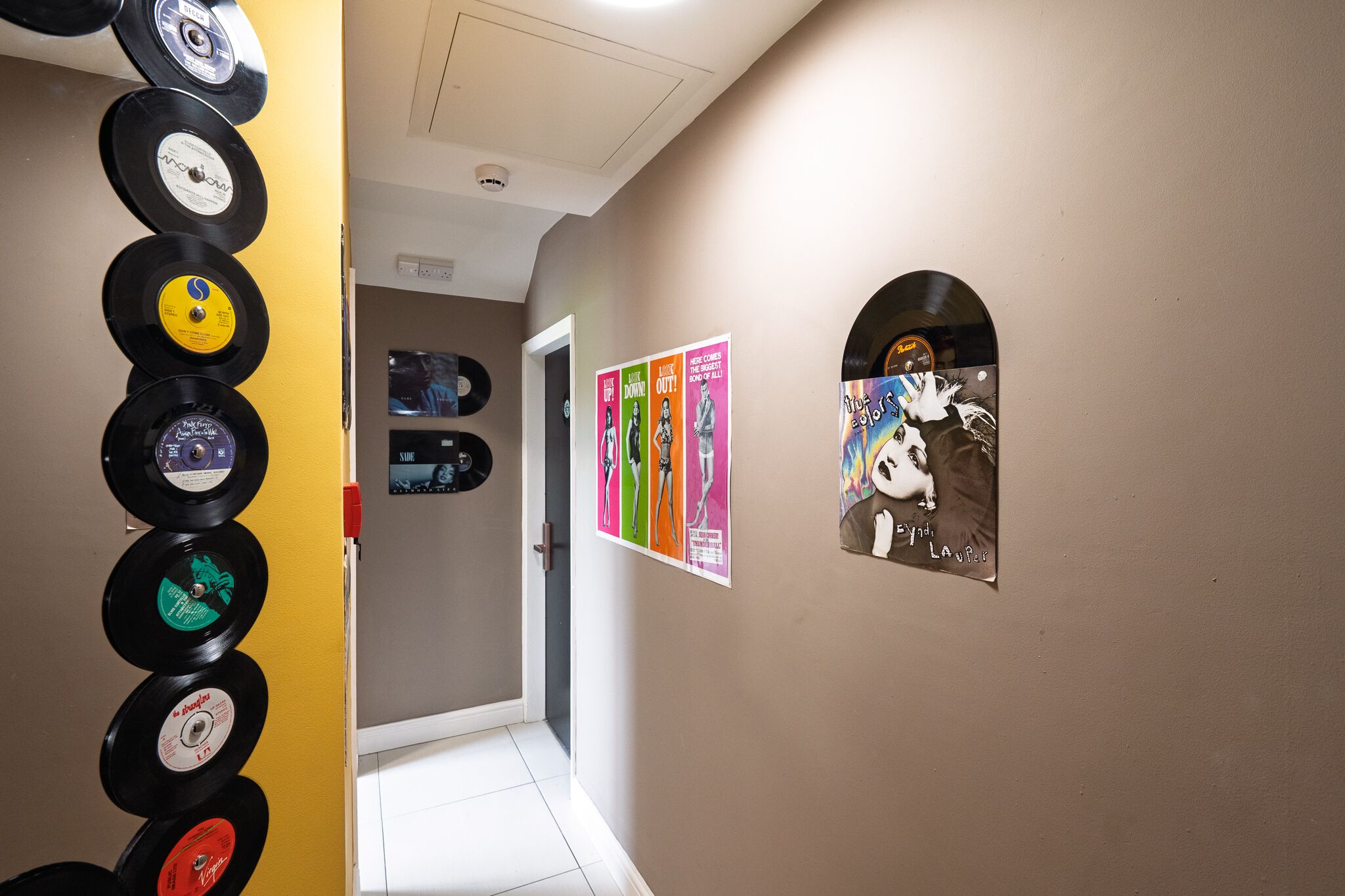 A hallway with vinyl records on the wall, a poster, and a framed picture.