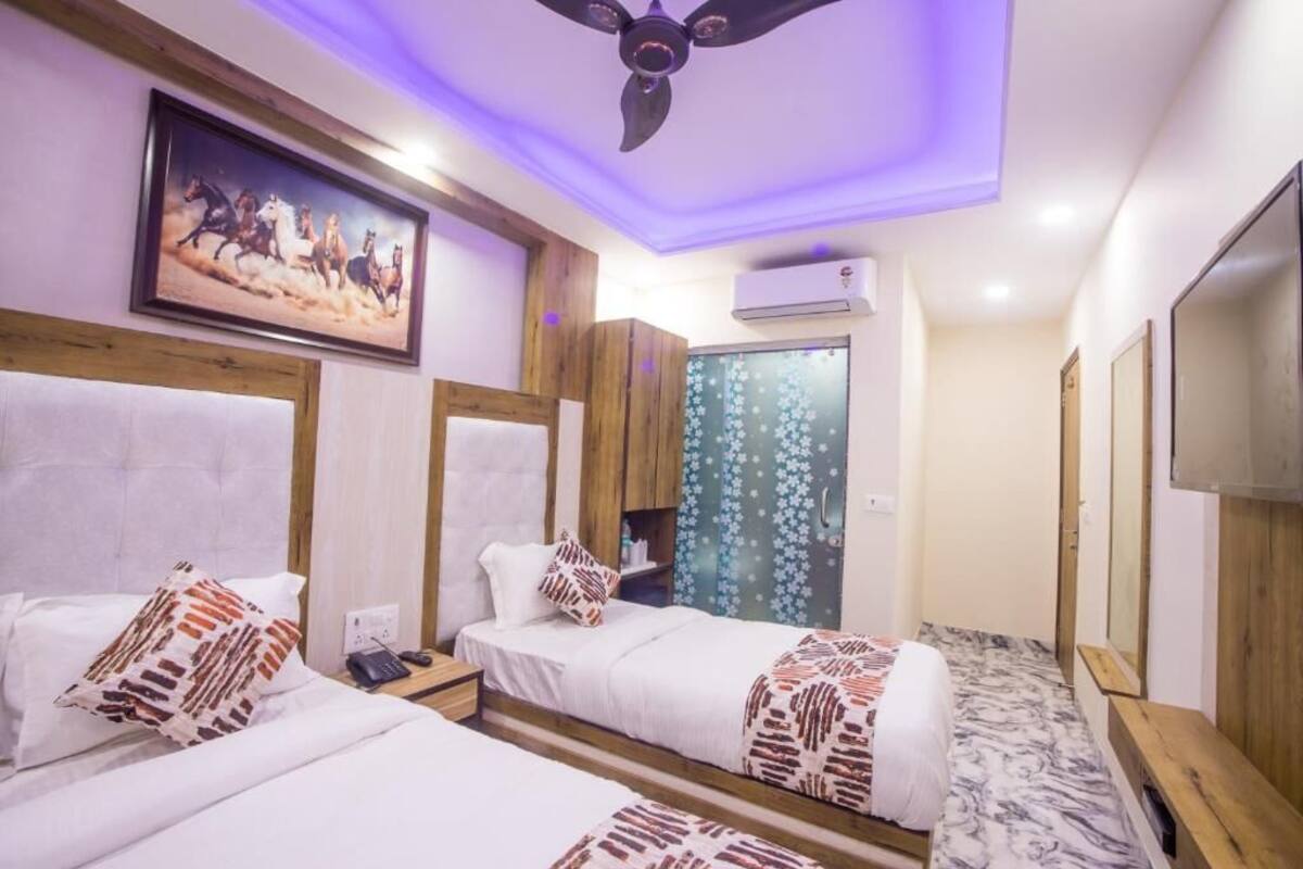 Ein Hotelzimmer mit zwei Betten, Holzkopfteilen, einem Deckenventilator, einer Klimaanlage, einem Fernseher und einer Tür mit Blumenmuster.