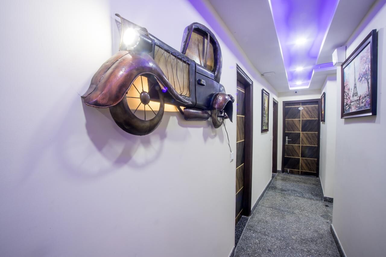 A hallway with a wall-mounted sculpture resembling a vintage car, a door with a patterned design, and framed artwork on the wall.