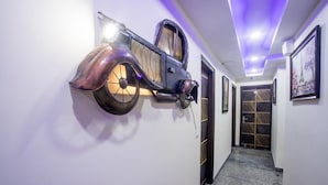 Un couloir orné d’une sculpture murale rappelant une voiture ancienne, d’une porte à motifs et de tableaux encadrés accrochés au mur.
