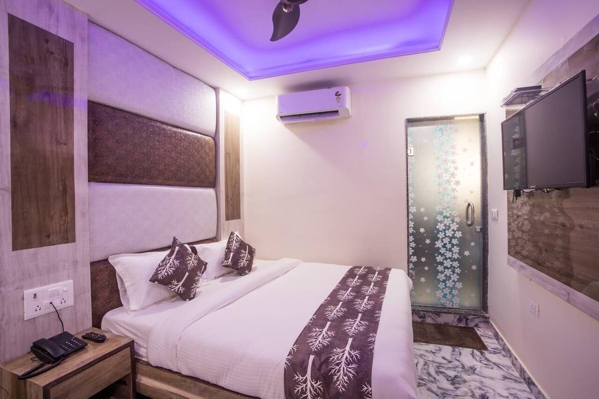 Ein Hotelzimmer mit Bett, Nachttisch mit Telefon und Fernbedienung, Klimaanlage, Fernseher und Dusche mit Milchglasüren.