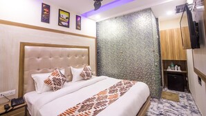 Une chambre d’hôtel avec un lit doté d’une tête de lit capitonnée, un ventilateur de plafond, un mur orné d’un motif en mosaïque, une petite kitchenette et un téléviseur.