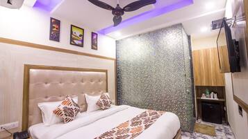 A hotel room with a tufted headboard bed, a ceiling fan, a wall with a mosaic pattern, a small kitchenette, and a television.