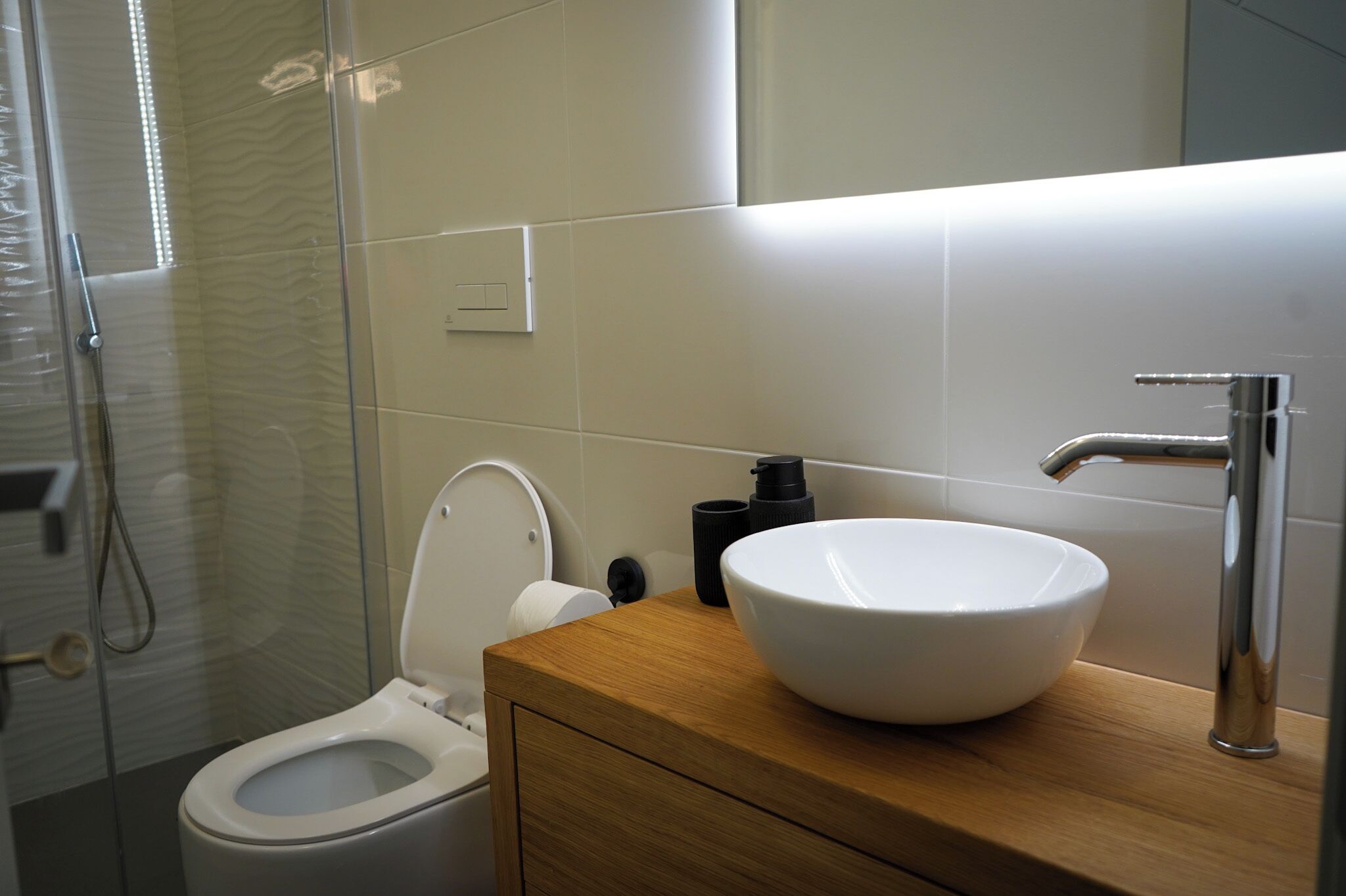 A modern bathroom with a white toilet, a wooden vanity with a white sink, and a shower area with a glass door.