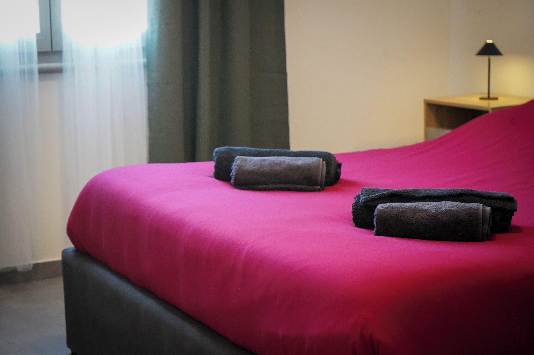 Un lit bien fait, avec une couverture rouge vif et deux serviettes pliées.