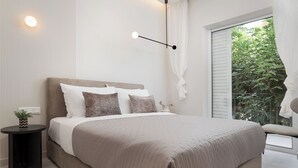 A modern bedroom with a large bed, a bedside table with a plant, and a view of greenery through a window. - Glyfada Prime Apartment, Glyfada Prime Living (Athens)