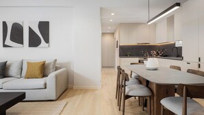 Ein modernes Wohnzimmer mit einer Couch, einem Couchtisch und einem Esstisch mit Stühlen. Es gibt eine Küchenzeile mit Arbeitsplatte und einer Pendelleuchte.