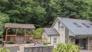 Une maison avec des fondations en pierre, une terrasse en bois et un espace extérieur aménagé et couvert.