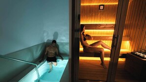 Een sauna met een glazen deur, houten banken en een zichtbare klok aan de muur.