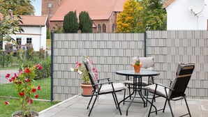 A patio with a table and chairs, a potted plant, and a brick wall.