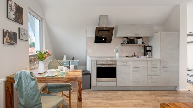 A modern kitchen with a built-in oven, microwave, and a stainless steel range hood. There is a dining area with a wooden table and chairs, and a window providing natural light.
