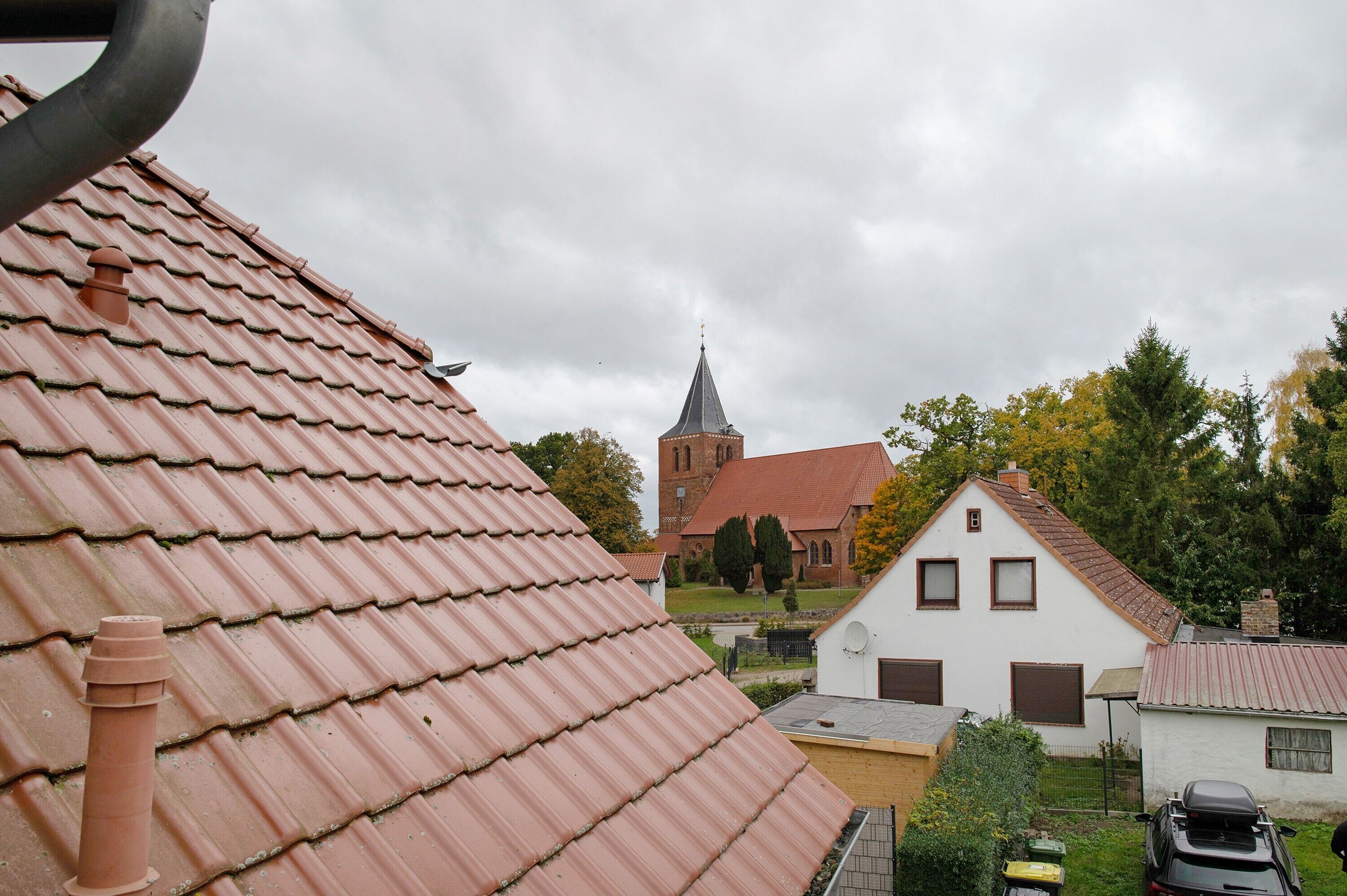 A residential area with a church, red-tiled roofs, and a white house with a garage.