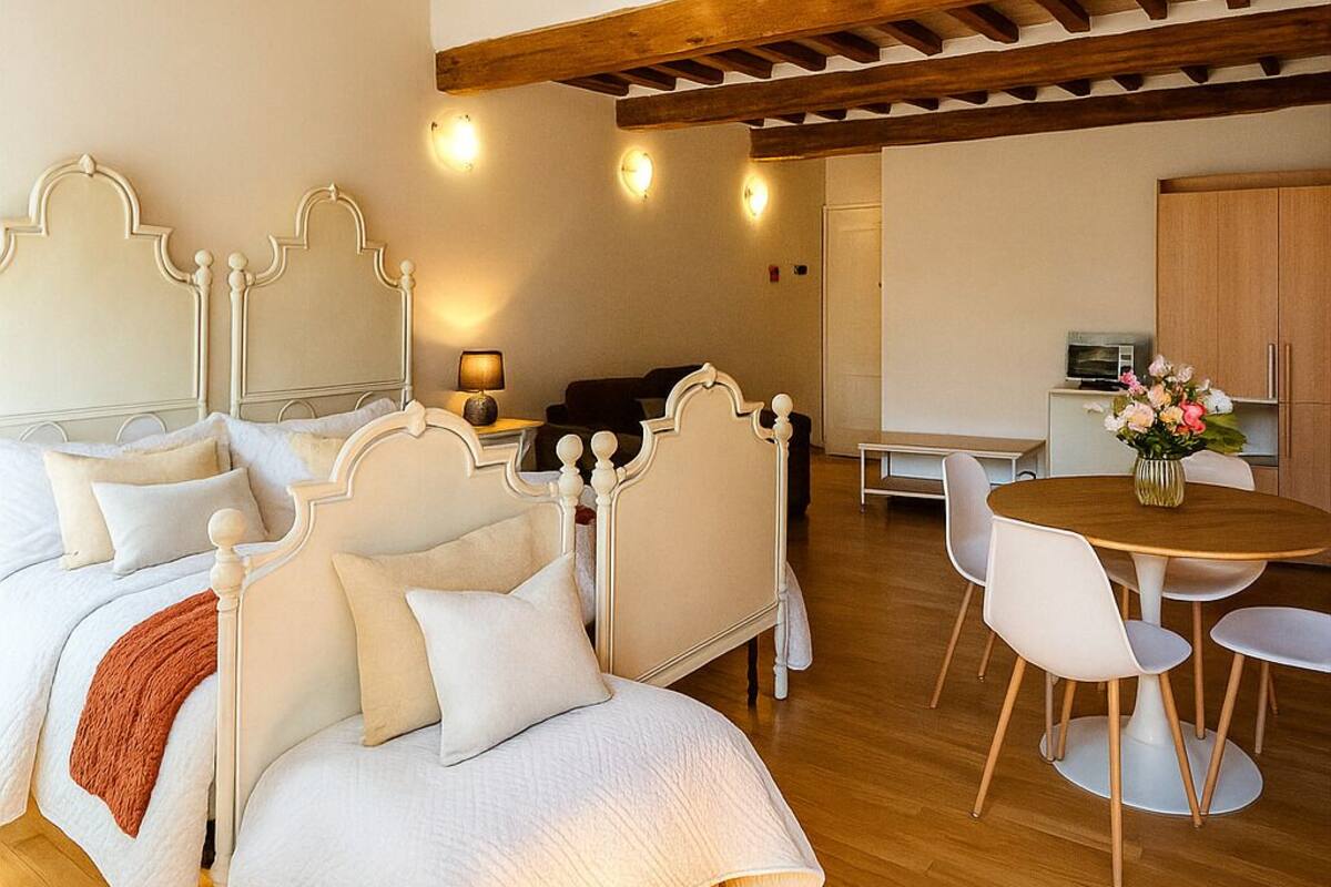 Ein Schlafzimmer mit einem großen Bett, Holzboden, einer Essecke mit Tisch und Stühlen sowie einer Küche im Hintergrund.