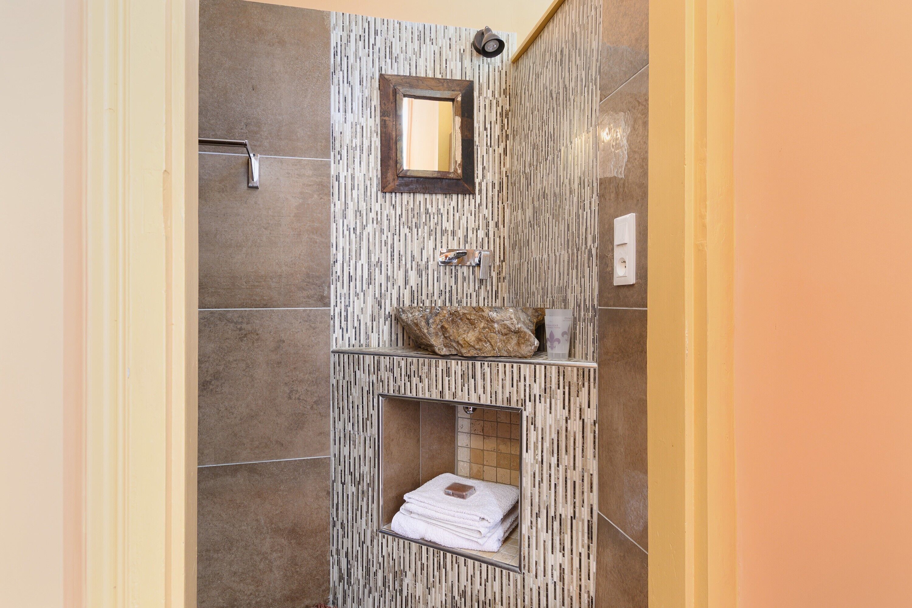 A bathroom with a tiled wall, a mirror, a sink with a soap dish, and a towel rack.
