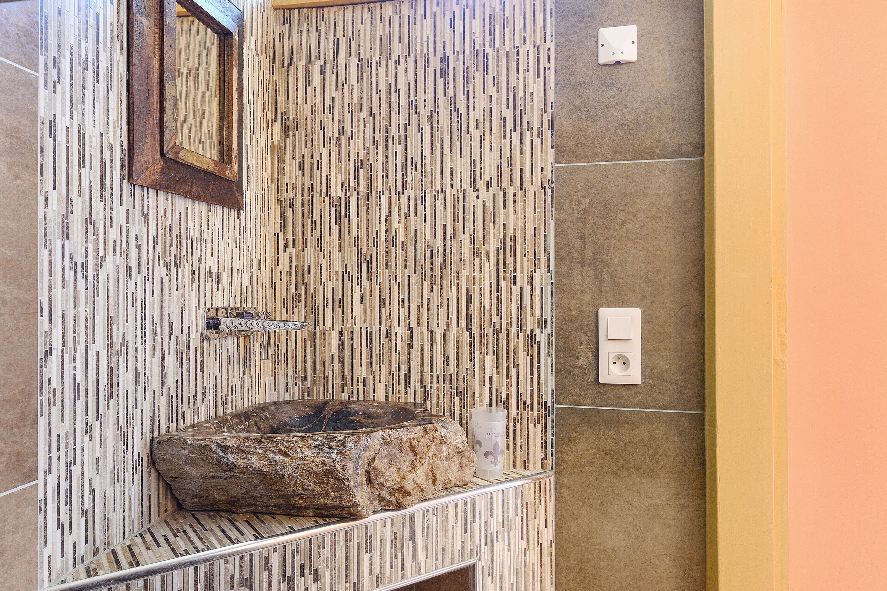 Un baño con pared de mosaicos, un lavamanos de piedra, un espejo y un perchero para toallas.