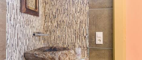 Ein Badezimmer mit einer Mosaikwand, einem Steinsinkens, einem Spiegel und einem Handtuchhalter.