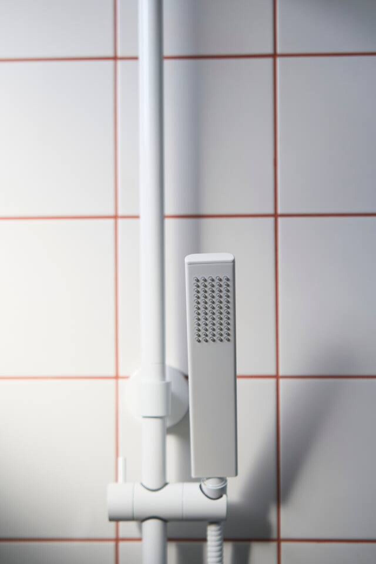 Un cabezal de ducha instalado en una pared blanca con azulejos formando un diseño de cuadrícula.