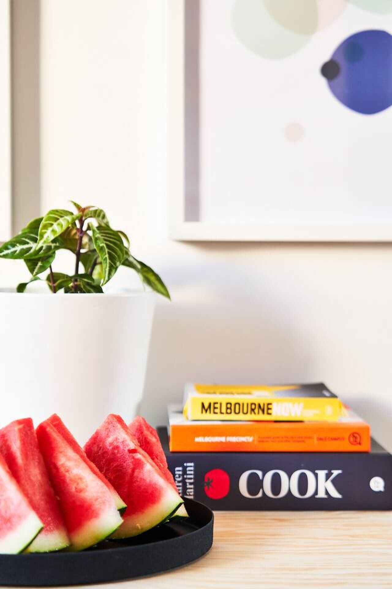 Ein Blumentopf, eine Schale mit Wassermelone und ein Stapel Bücher auf einem Tisch.