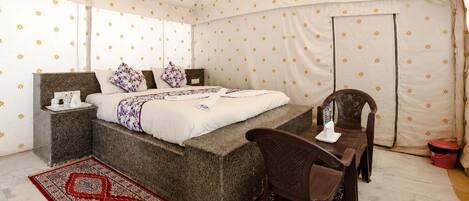 A tented room with a bed, bedside table, chair, and a red patterned rug.