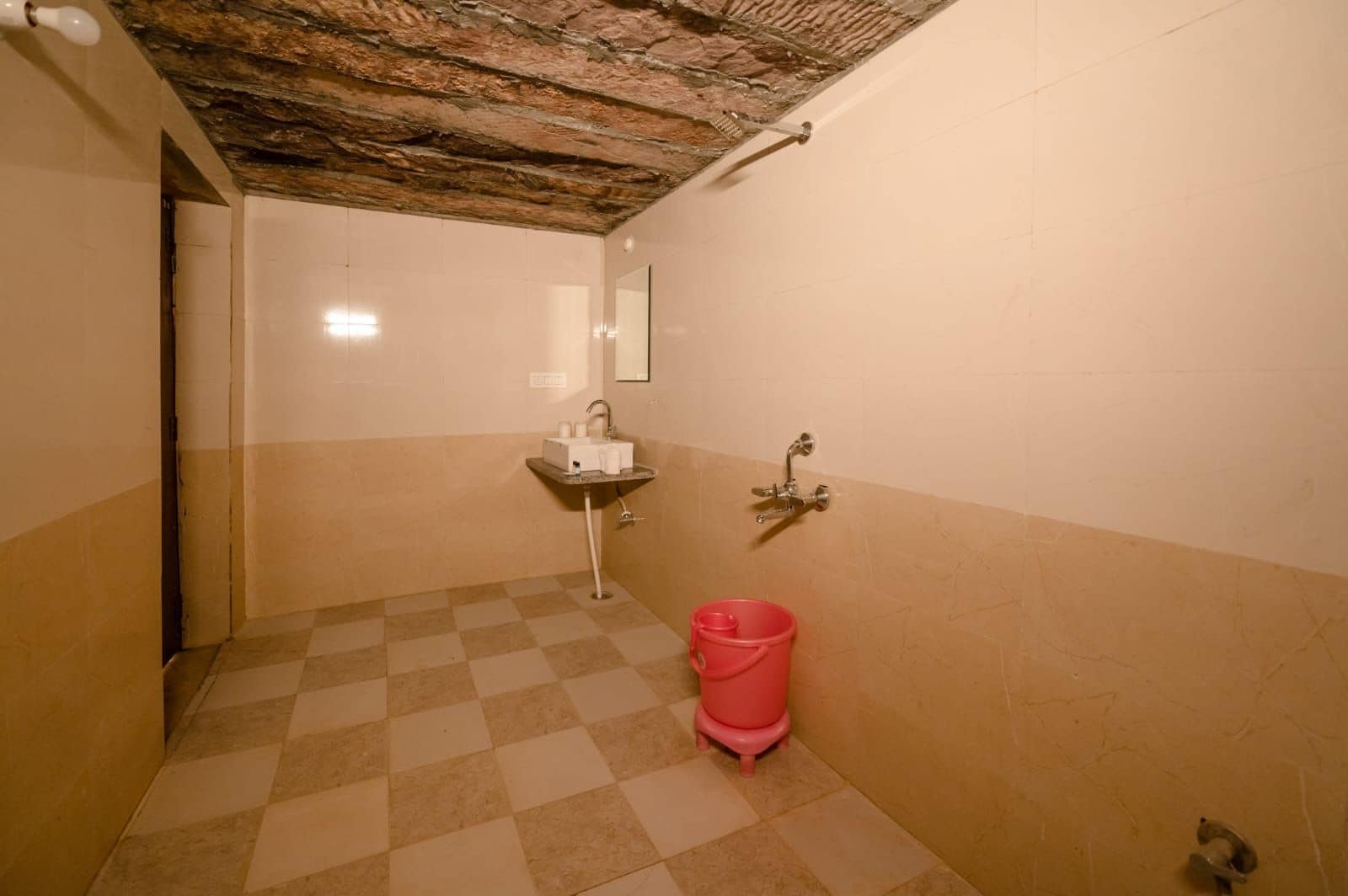 Un baño con piso a cuadros, un lavamanos, un espejo y un balde rojo.