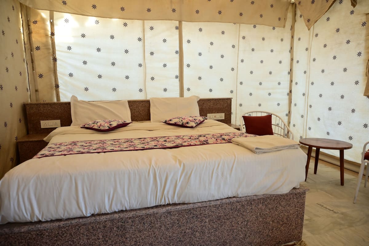 Una cama con colcha floral, un cojín rojo y un cabecero de madera.