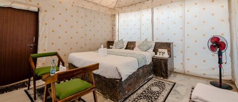 A tented room with a bed, a chair, a bedside table, a fan, and a door.