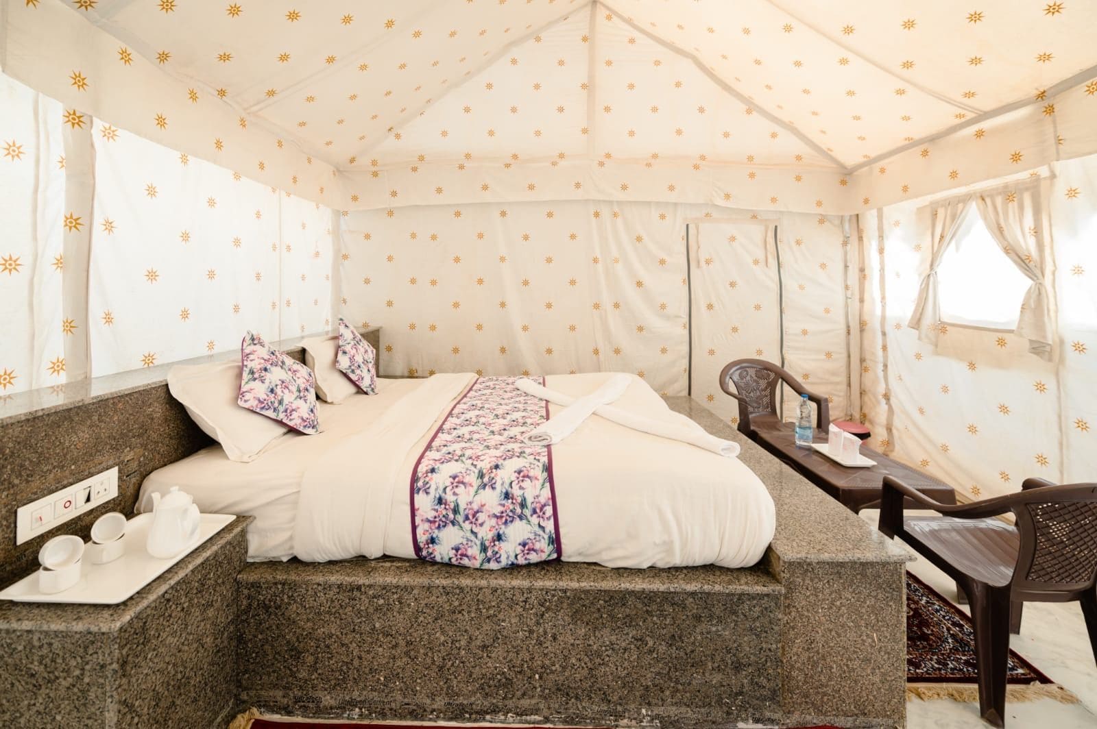 A tent-style room with a bed, a small table with a chair, and a window.