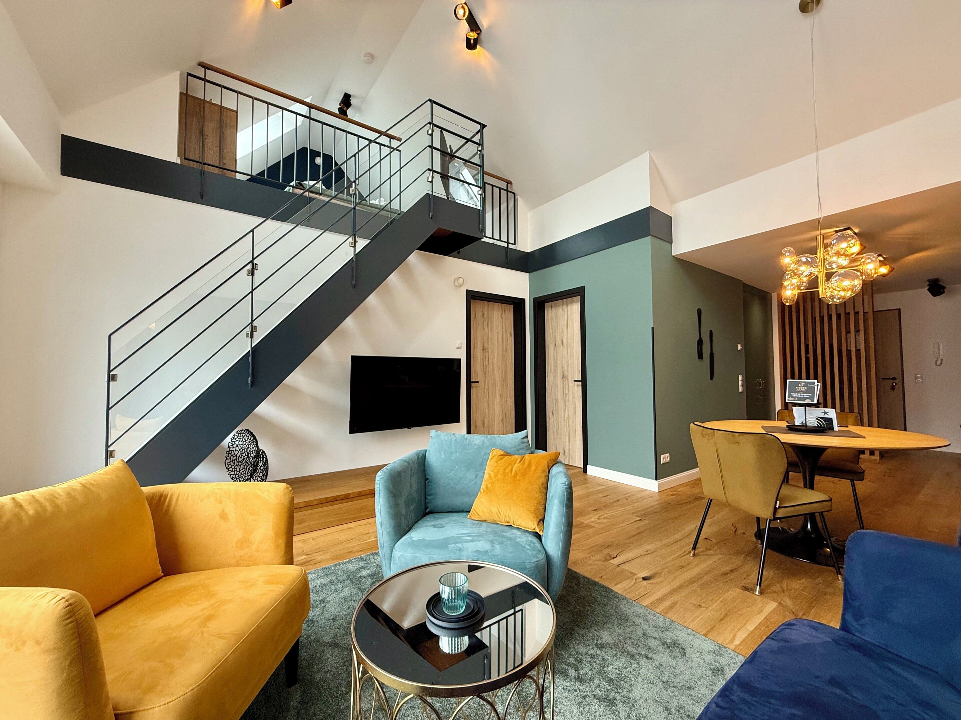 A modern living room with a staircase, a flat-screen TV, and a dining area with a table and chairs.