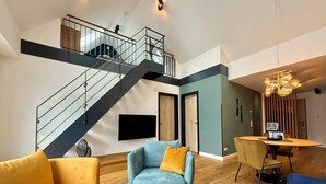 A modern living room with a staircase, a flat-screen TV, and a dining area with a table and chairs. - Completion 2025: Modern apartment with sauna and private balcony! (Sankt Peter-Ording)