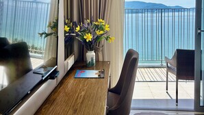 A hotel room with a wooden table, a TV, a vase with flowers, and a balcony with a view of the sea.