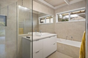 Een moderne badkamer met een douchecabine van glas, een witte wastafel en een bad.